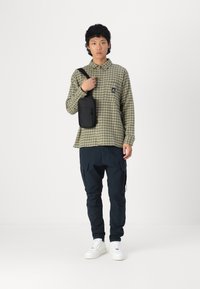 Green and beige checkered shirt, black crossbody bag, navy cargo pants, and white sneakers. Casual fit, buttoned shirt, cargo pockets on pants.