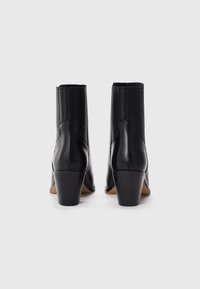 Botas de tobillo de cuero negro con un parte superior texturizada, paneles laterales elásticos y un tacón bloque de altura media. Acabado suave con un detalle minimalista.