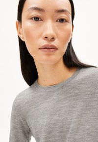 Grauer Strickoberteil mit rundem Ausschnitt, weicher Textur und langen Ärmeln. Der Stoff scheint leicht und weist subtile Farbvariationen auf.