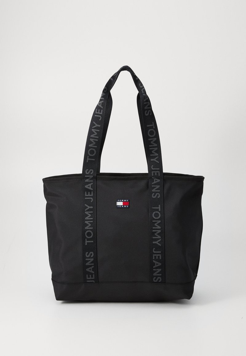 Čierna taška cez rameno z odolného materiálu s logom, širokými popruhmi a značkovým označením "TOMMY JEANS". Obdĺžnikový tvar so zipsom.