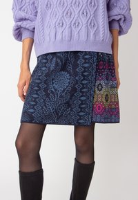 Jupe en mélange de laine avec une base bleu marine foncé ornée de motifs floraux bleus complexes et de designs géométriques vifs en rose, bleu et jaune.