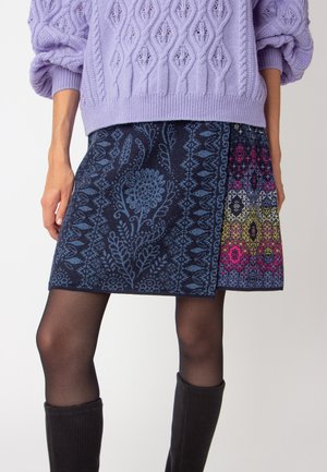 Jupe en mélange de laine avec une base bleu marine foncé ornée de motifs floraux bleus complexes et de designs géométriques vifs en rose, bleu et jaune.