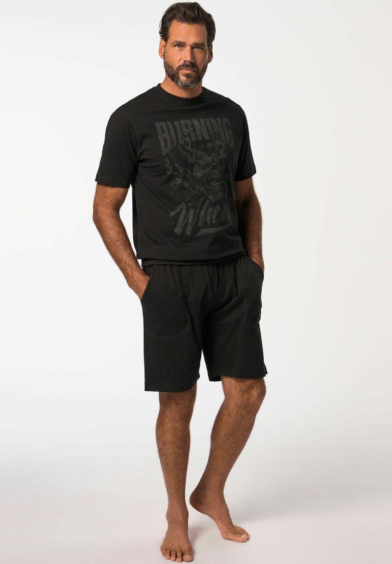 Camiseta de algodón negra con un estampado gráfico, combinada con pantalones cortos negros. Ambos prendas presentan un corte relajado y un diseño casual.