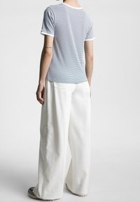 Camiseta de rayas azul claro con detalles blancos y mangas cortas, combinada con pantalones anchos blancos, vista desde atrás.