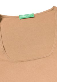 Top in cotone color sabbia con scollatura a barca. Presenta una texture liscia e una leggera elasticità. L'etichetta riporta "United Colors of Benetton" in verde.