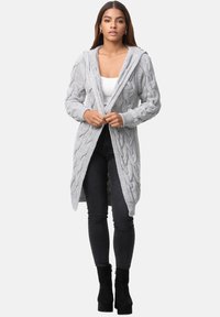 Cardigan lungo in maglia a cavo grigio chiaro con cappuccio, apertura frontale e polsini a costine, abbinato a jeans neri aderenti e stivali neri con tacco.