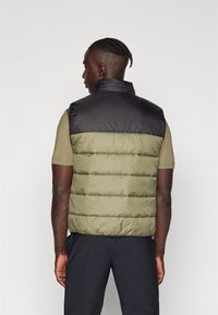 Gilet matelassé avec une partie inférieure verte et une section supérieure noire, doté d'un col haut et d'un design cousu. Porté sur une chemise à manches courtes.