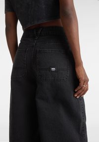 Jeans in denim nero con vita alta, gambe larghe e un'etichetta cucita a contrasto sulla tasca posteriore. Tessuto testurizzato con una leggera lucentezza.