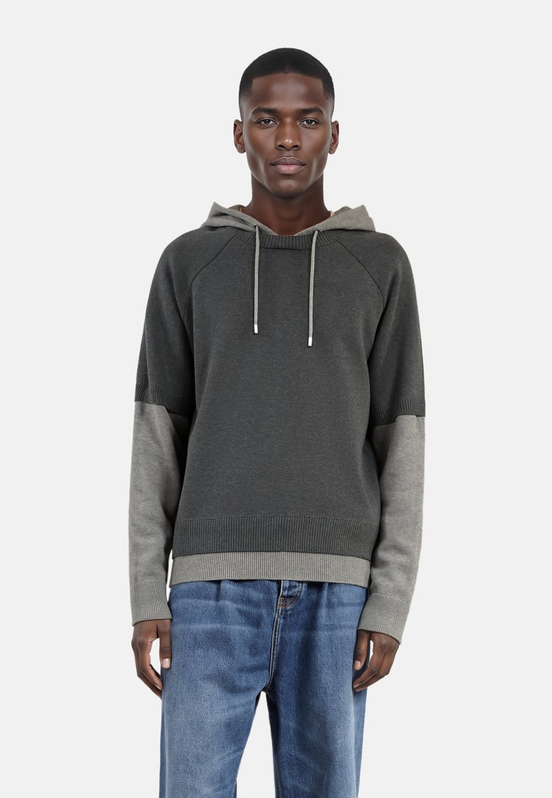 Felpa grigia con un accento grigio più chiaro sulle maniche. Caratterizzata da un ampio cappuccio, orlo e polsini a costine, e cordini regolabili. Indossata con jeans blu.