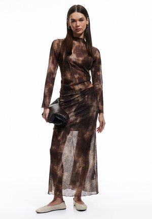 Top a maniche lunghe marrone tie-dye abbinato a una gonna coordinata. L'outfit presenta un tessuto trasparente ed è completato da una borsa nera strutturata.