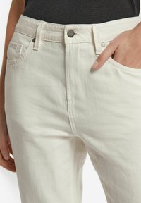Vita denimjeans med en slät textur, med dragkedja, metallknappstängning och framfickor. Synliga sömmar och detaljer i stygn.