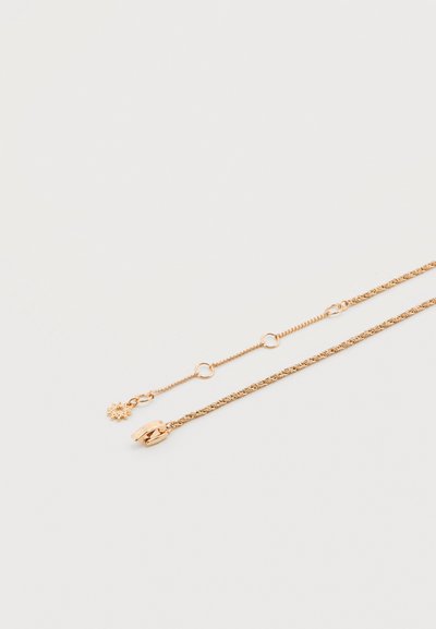 Δύο λεπτές χρυσές αλυσίδες με διαφορετικούς κούμπους και μικρές λεπτομέρειες με κρίκους, η μία με ένα μικρό μενταγιόν σε σχήμα ήλιου, σε ανοιχτό φόντο.