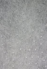 Tissu en denim gris avec un motif de tissage diagonal parsemé de petits clous argentés réfléchissants, répartis de manière uniforme sur toute la surface.