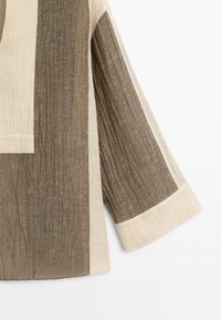 Overhemd met lange mouwen met brede bruine en beige verticale panelen en een gestructureerd stofpatroon op een witte achtergrond.