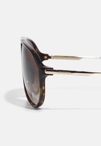 Skildpaddemønstrede solbriller med et elegant design, mørke linser og guldfarvede metalaccenter på stængerne. Glat tekstur og moderne form.