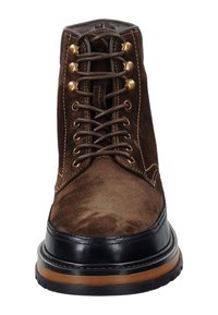 Hnědé semišové kotníkové boty s černými koženými detaily, kovovými očky a hnědými tkaničkami. Mají kulatou špičku a texturovanou podrážku.