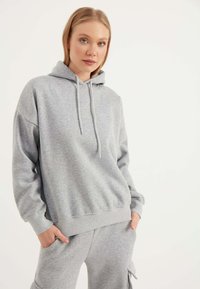 Grau Kapuzenpullover mit lässiger Passform, ausgestattet mit einer Kängurutasche und einer Kordelzug-Details. Weicher Stoff mit gerippten Bündchen und Saum.