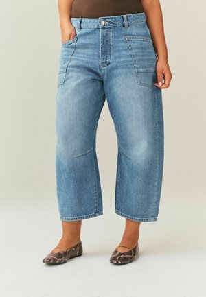 Jean bleu clair à jambe large et longueur raccourcie avec de grandes poches plaquées à l'avant, porté avec des ballerines marron en similicuir peau de serpent.