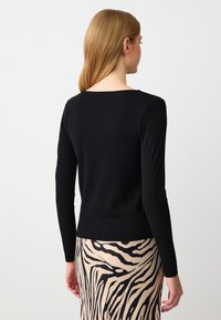 Zwarte geribbelde top met lange mouwen en een vierkante halslijn, gecombineerd met een beige rok met een zwart zebra-streeppatroon.