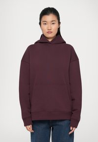 Felpa bordeaux con grande tasca a marsupio, vestibilità oversize e cappuccio foderato. Tessuto morbido con polsini e orlo a coste.