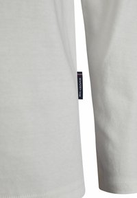 Weißes Baumwoll-T-Shirt mit rundem Halsausschnitt, kurzen Ärmeln und einem kleinen marineblauen Etikett mit roten Akzenten an der Seitennaht. Glatte Textur.