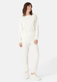 Felpa bianca e pantaloni coordinati in morbido tessuto, con colletto a girocollo, polsini a coste e rifiniture decorative sul cinturino.