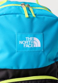 Μπλε και μαύρο σακίδιο με φωσφορίζον κίτρινες ταινίες φερμουάρ και μπατς με το λογότυπο The North Face ραμμένο στο μπροστινό μέρος.