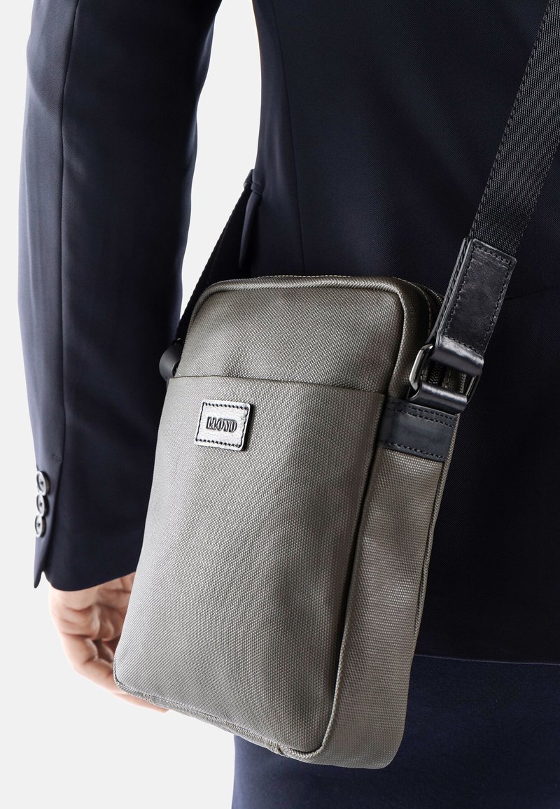 Borsa a spalla grigia in tessuto con superficie texture, caratterizzata da un accento in pelle, tracolla regolabile e una patch con logo sul davanti.