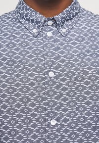 Šedá košile na knoflíky s vzorem diamantů a trojúhelníků v bílé barvě; měkká textura s klasickým límcem a plastovými knoflíky.