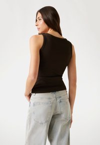 Schwarzes, geripptes Tanktop mit enganliegendem Schnitt, kombiniert mit hellblauen, locker sitzenden Jeans mit aufgesetzten Taschen und einem Logostick.
