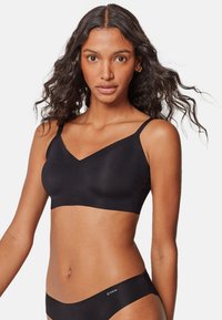 Soutien-gorge sans fil noir avec un design en V et des bretelles réglables. Texture lisse, construction sans couture. Détail du logo sur le côté.