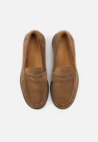 Καφέ μοκασίνια από σουέτ με στρογγυλερή μύτη, διαθέτουν διακοσμητική ραφή στο επάνω μέρος και διακριτικές λεπτομέρειες. Εξωτερική σόλα από καουτσούκ για κράτημα και ανθεκτικότητα.