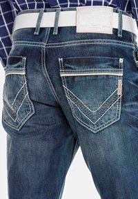 Donkerblauwe denim jeans met contrasterende witte stiksels, met twee achterzakken voorzien van ruitvormige ontwerpen en een witte rechthoekige leren patch.