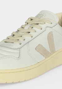 Λευκό δερμάτινο αθλητικό παπούτσι με μπεζ σουέντ λογότυπο "V" στο πλάι, κρεμ κορδόνια και μπεζ σόλα, που δείχνει ραμμένες λεπτομέρειες και σήμανση στη γλώσσα.