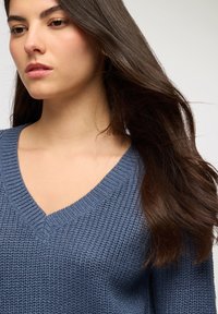 Niebieski sweter pleciony z dekoltem w kształcie litery V, posiadający ribbowany kołnierz, z teksturowaną powierzchnią i luźnym krojem.
