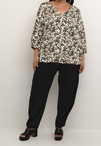 Bluse med blomsterprint, V-hals, trekvartærmer og en afslappet pasform, parret med sorte, løst siddende bukser og kraftige hælsandaler.