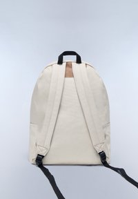 Béžový látkový batoh s černými popruhy, horní rukojetí a hnědým akcentem. Hladká textura a zaoblený tvar s nastavitelnými popruhy.