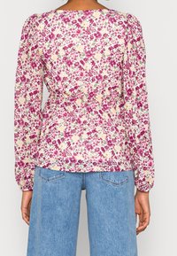 Femme portant un chemisier à manches longues rose et beige à motifs floraux, rentré dans un jean taille haute bleu clair, vue de dos.