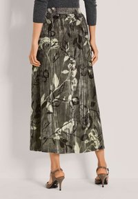 Maxi rok in het groen met een bloemenprint. Heeft een gerimpelde taille, geplooide textuur en valt tot halverwege het kalf. Draagt met hoge sandalen.