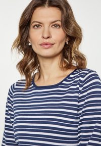 Maglia a maniche lunghe a righe navy e bianche con scollatura rotonda e un tessuto morbido e testurizzato. Presenta una vestibilità rilassata e cuciture in vista.