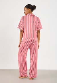 Red and white striped cotton pajama set with a short-sleeve button-up top and long pants featuring a relaxed fit and black piping accents.