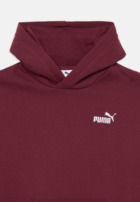 Burgunder hettegenser med teksturert stoff. Har en hvit Puma-logo på brystet og en romslig frontlomme.