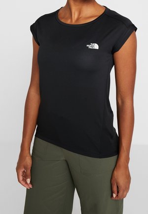 Vrouw draagt een zwart mouwloos T-shirt van The North Face en olijfgroene broek, staand tegen een effen achtergrond.