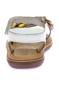 Sandalia marrón y blanca con tres correas ajustables, material de cuero, acentos florales, suela texturizada y plantilla con marca.