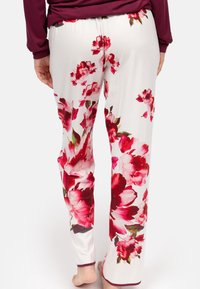 Bloemenbroek van zacht materiaal, met grote rode en roze bloempatronen op een witte achtergrond en een elastische tailleband.