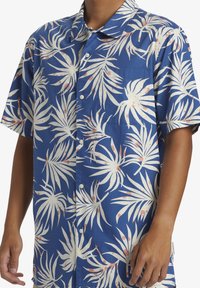 Camisa de botonadura corta en azul con un patrón de hojas de palmera en blanco y rosa. Fabricada en tejido ligero; cuenta con un bolsillo en el pecho.