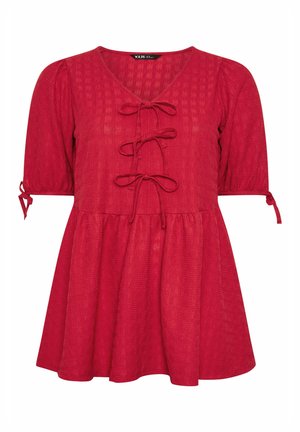 Blouse rouge texturée à manches courtes avec encolure en V, trois fermetures à nouer à l'avant, manches bouffantes et petits nœuds aux poignets.