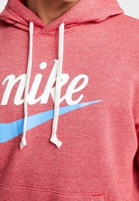 Röd fleecehuva med vita dragsnören, med fet vit "nike" text och en ljusblå swoosh-design över framsidan.