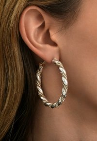 Boucle d'oreille en argent torsadée avec une finition polie, présentant des détails complexes et un système de fermeture sécurisé pour un port confortable.
