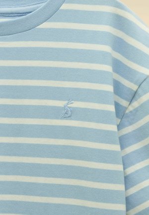 Blau-weiß gestreifter Stoff mit einem kleinen, auf der Brust eines Kleidungsstücks aufgestickten blauen Hasenlogo.